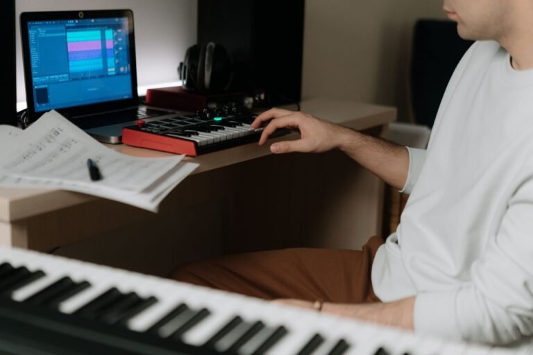 A person working on music production using a MIDI keyboard and laptop in a home studio.